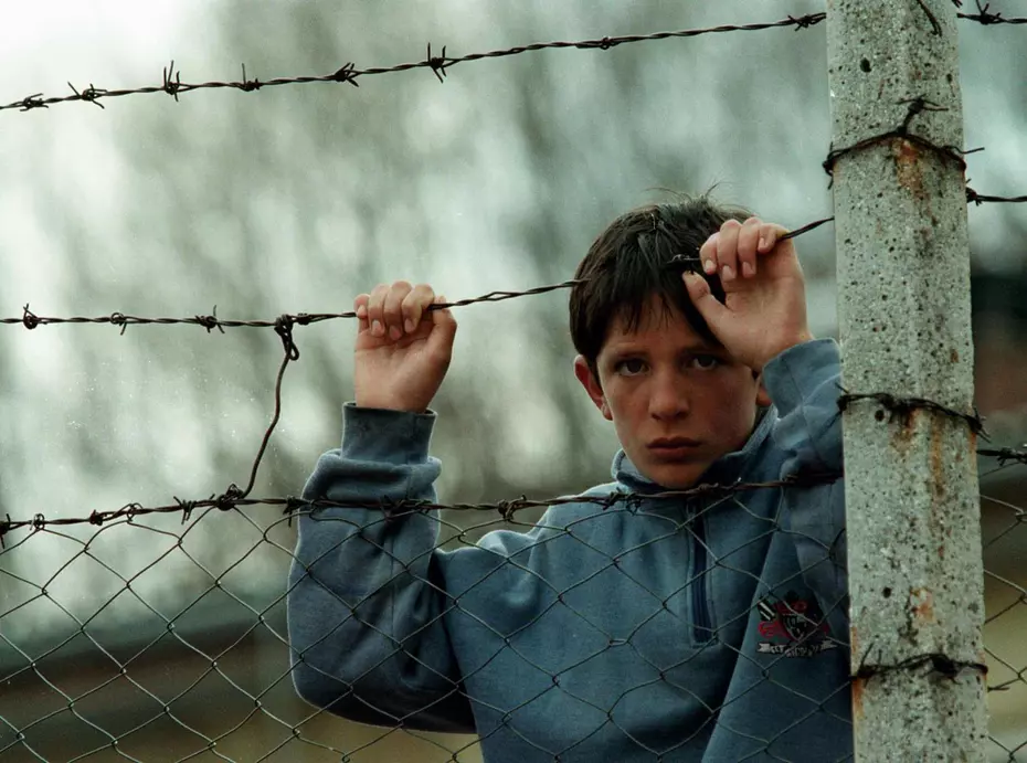 Un ragazzo che si aggrappa a una recinzione di filo spinato durante il conflitto in Kosovo nel 1999 – simbolo di difficoltà e speranza sostenuta dalla Catena della Solidarietà.