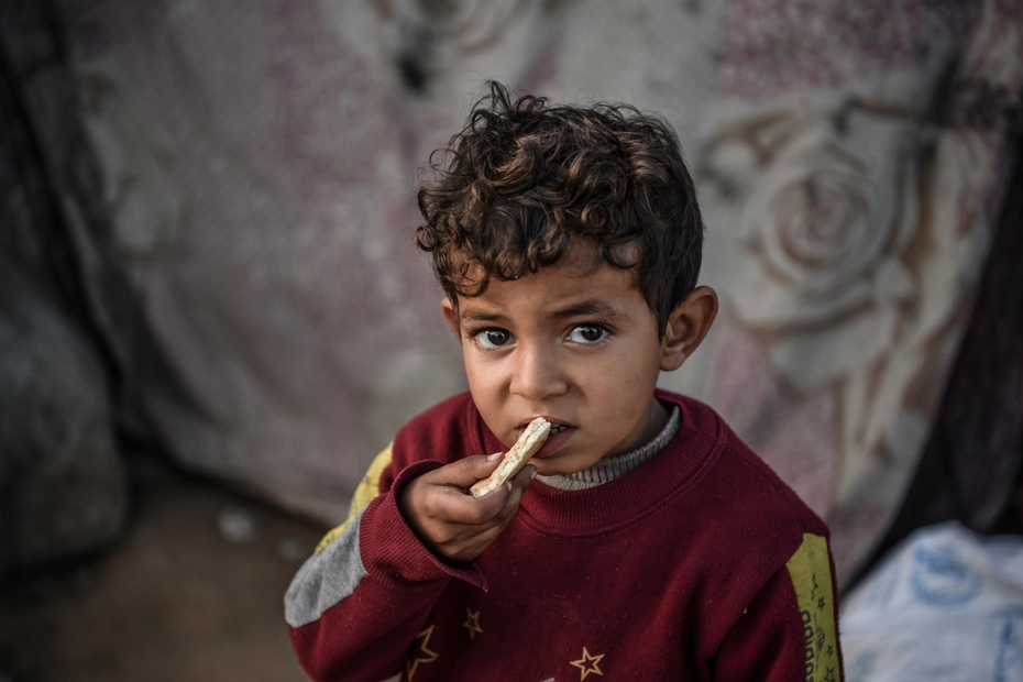 Un bambino con un pezzo di pane Un bambino mangia un pezzo di pane: le donazioni forniscono aiuti alimentari essenziali in tempo di guerra.