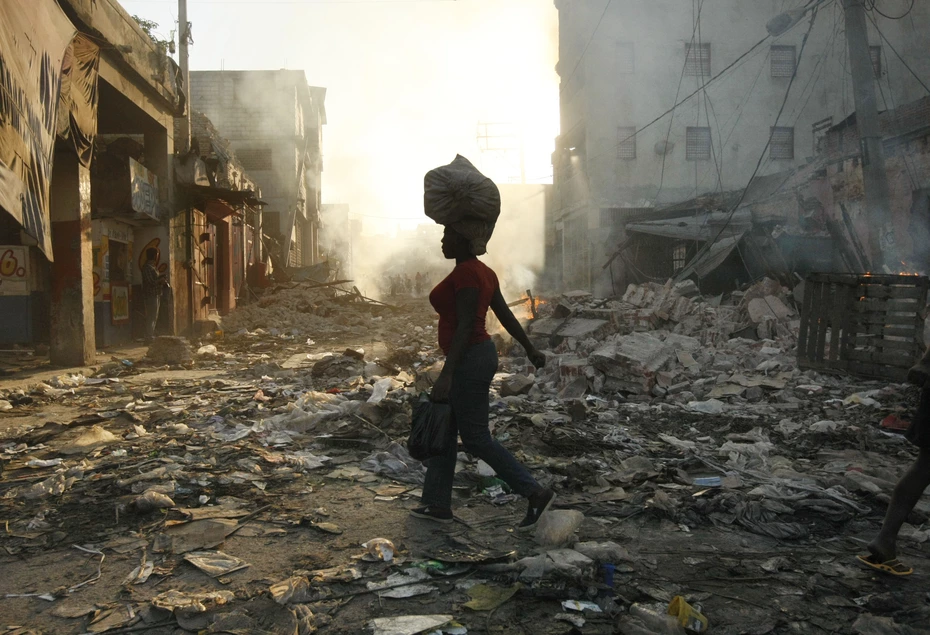 Una donna cammina attraverso una città distrutta ad Haiti con una borsa sulla testa al tramonto, dopo il terremoto del 2010 sostenuto dalla Catena della Solidarietà.