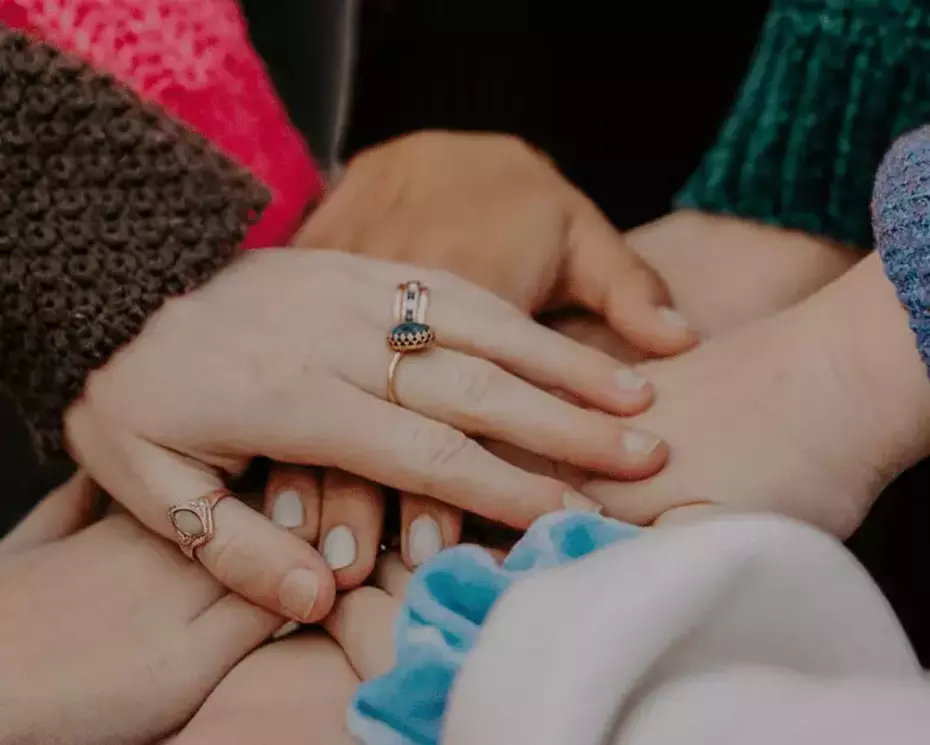 Le mani sovrapposte illustrano la solidarietà, l'impegno collettivo e il sostegno umano.