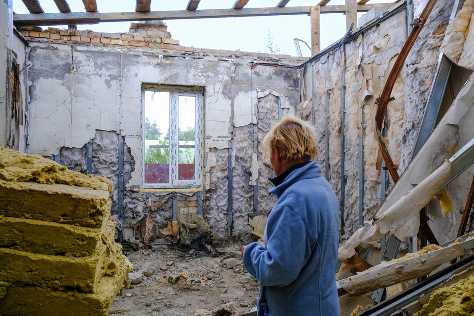 Una persona all’interno di una casa bombardata in Ucraina guarda in una stanza distrutta – simbolo dell’impatto della guerra sui civili.