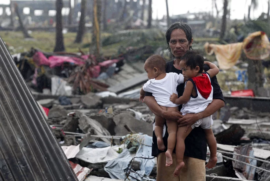 Un uomo sorride stringendo due bambini tra le macerie causate dal tifone Haiyan nel 2013, simbolo di resilienza e speranza.