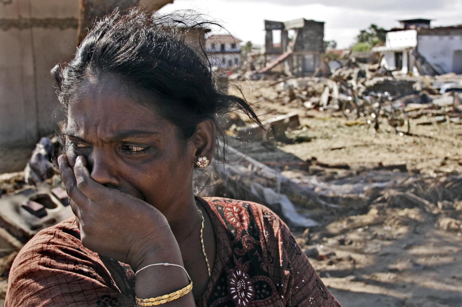 Una donna con le lacrime agli occhi guarda altrove, davanti a un paesaggio devastato dopo lo tsunami del 2004 nel Sud-est asiatico.