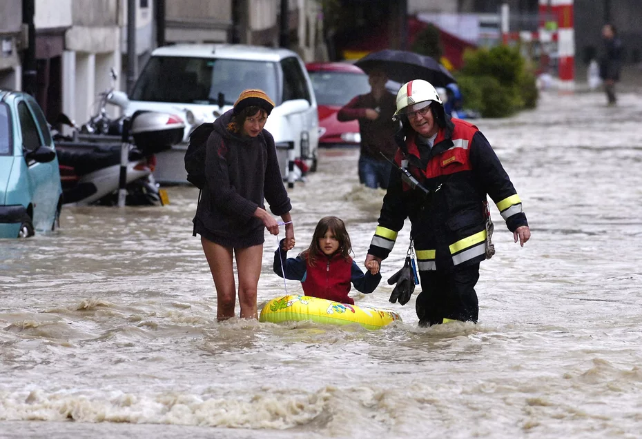 Un uomo e una donna tengono la mano di una bambina seduta su un gommone giallo mentre camminano tra strade allagate durante le alluvioni in Svizzera nel 2005.
