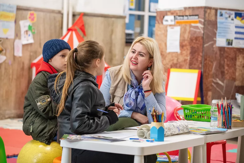 L' educazione nonostante la guerra in corso Un insegnante e due bambini in un'aula scolastica colorata - accesso all'educazione per i bambini sfollati in Ucraina nonostante la guerra.