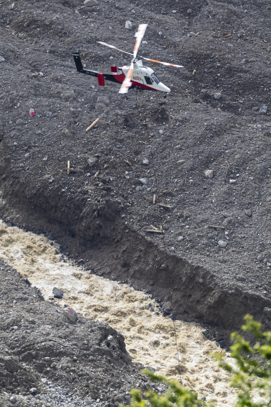 Trasporto aereo a Blatten: assistenza dal cielo dopo la frana Elicottero in azione su detriti e torrente a Blatten - assistenza rapida dopo la frana, urgono donazioni.